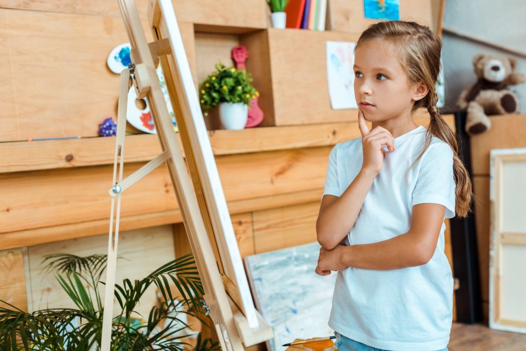 pensive kid looking at easel in art school